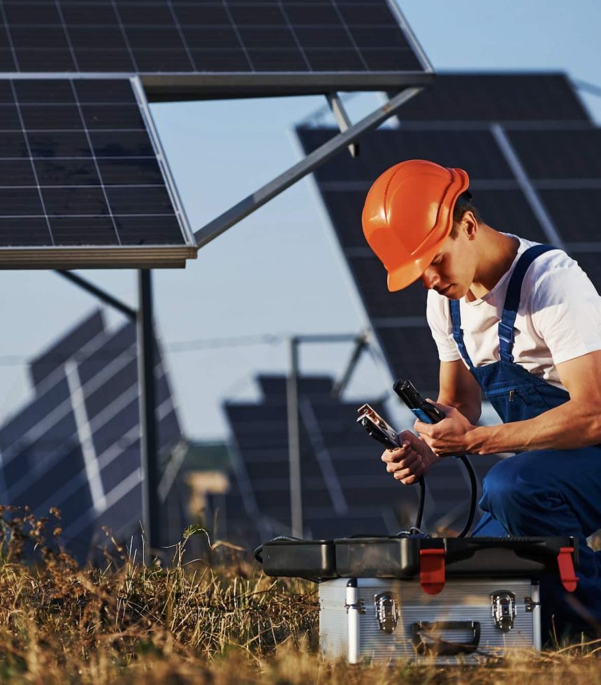 Male worker in blue uniform outdoors with solar batteries at sunny day